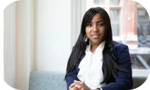This is a photo of a woman with long dark hair, wearing a navy blazer and white blouse, sitting indoors near a window.