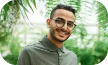 A photo of a person with glasses and a beard, smiling in a lush, green outdoor setting with leafy plants in the background.
