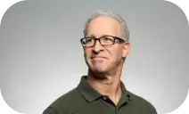 A portrait photo of an older man with glasses and short gray hair, wearing a dark green polo shirt, and gazing slightly to the side.